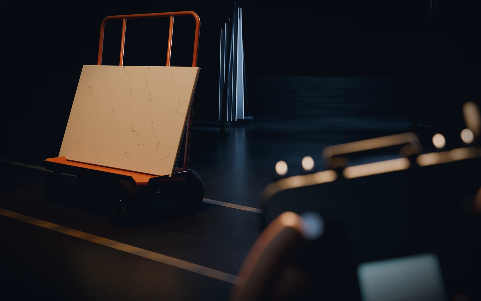 A dark shop floor with yellow lines: an orange drywall cart carries a slab of white marble past racks of stone, and in the foreground, out of focus, a hand holds the radio transmitter that drives it